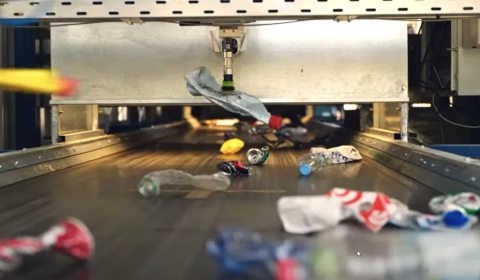 Plastic bottles on a conveyor belt, one being picked up by a machine