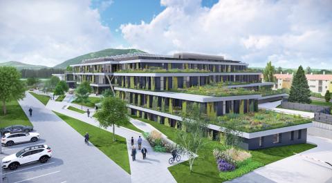 A 4-storey building with green roofs and grass around it, with people walking around, trees and a few cars