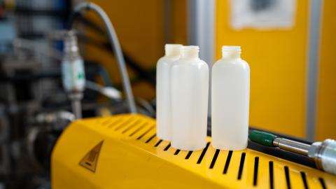 3 bottles made out of a plastic-looking material sitting on yellow machinery