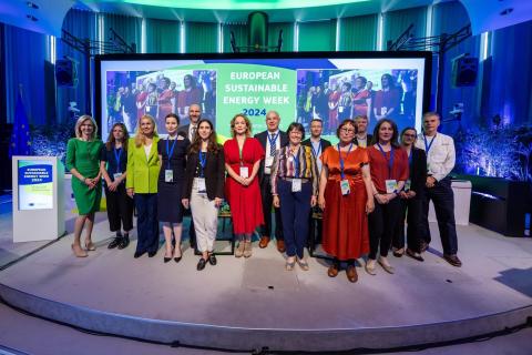 Delegation on a stage in front of screen with the writing "European Sustainable Energy Week 2024"
