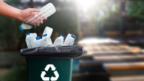 A rubbish bin with plastic bottles in it and a recycling logo on the side