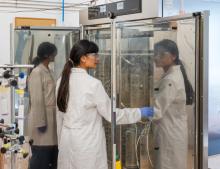 Woman in a lab coat with her hand in a cupboard with tubes and canisters