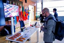Man looking at a booth with leaflets, with a screen and flags behind it