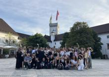 Group of around 40 young people in a town square, with old white buildings and a clock tower behind them   