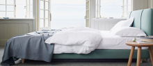 A bed with mattress with duvet, pillows and sheets