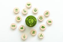 Green ball in the middle of a series of wooden buttons with logos relating to various parts of the circular economy, for example: renewable energy, working together, recycling, industry etc.