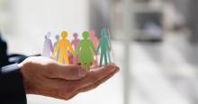 Hands holding multicoloured person paper cutouts linked by their hands and standing in a circle